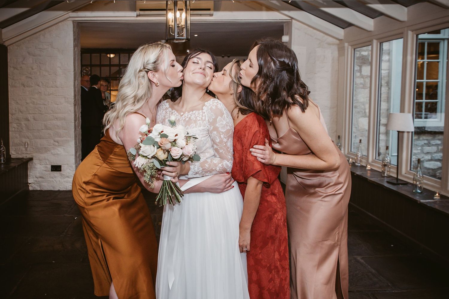 Wedding party in silk autumn-colored dresses share intimate moment during photo session.