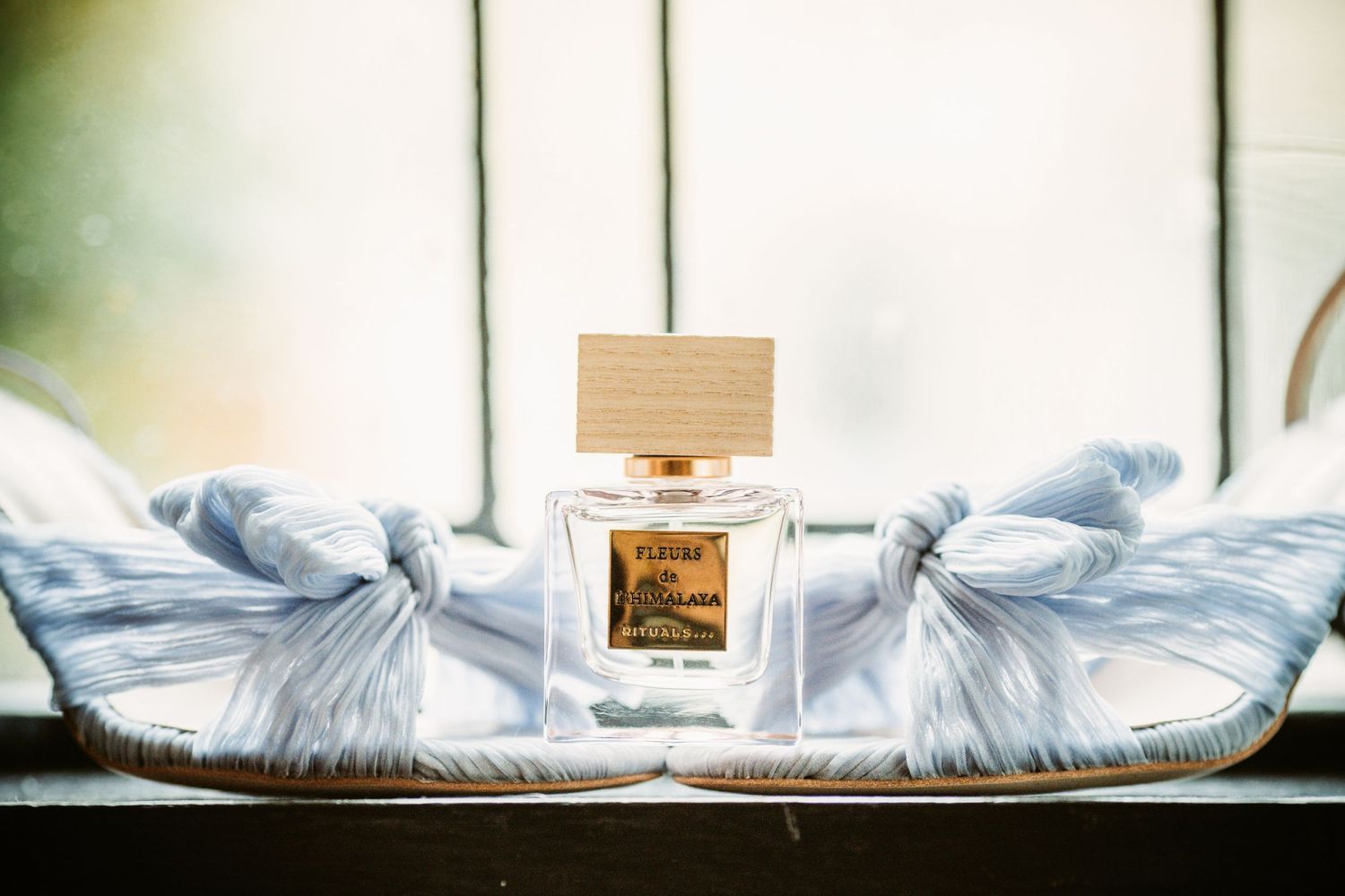 Perfume bottle arranged with light blue fabric on windowsill.