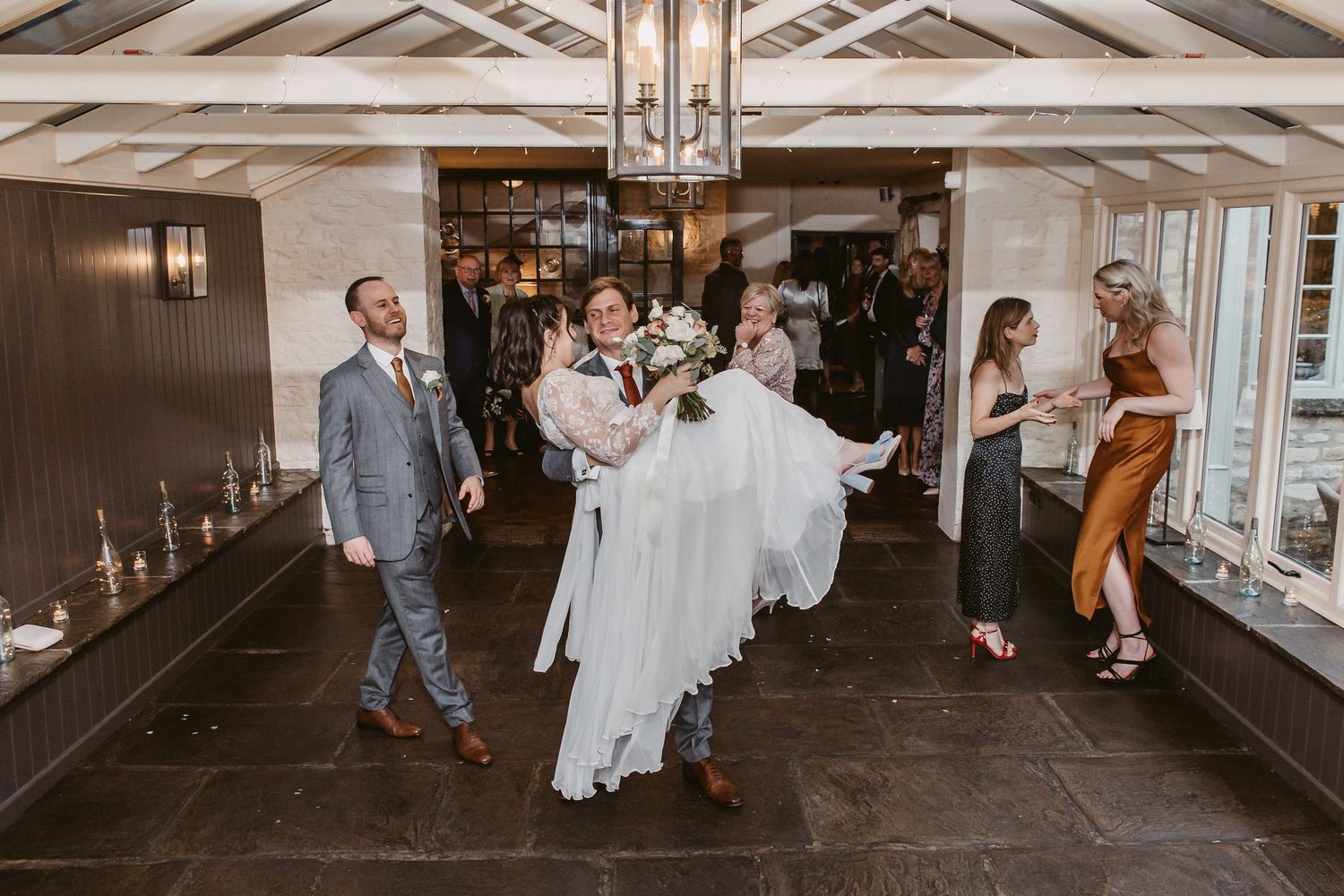 Wedding celebration with guests watching as couple is carried across reception venue floor.