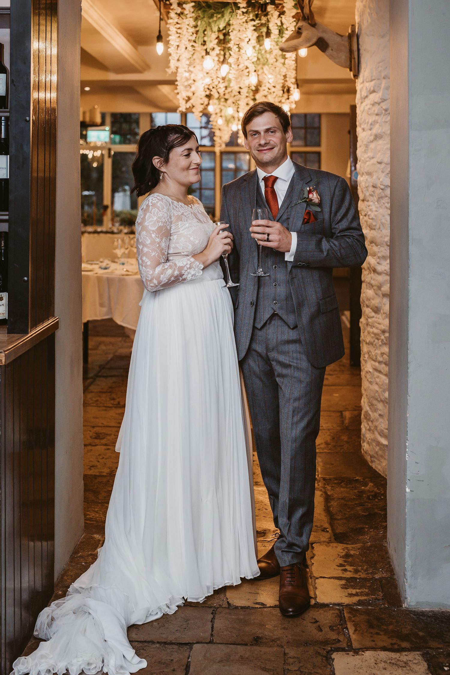 A newlywed couple enjoys champagne together under decorative lighting in an elegant venue hallway.