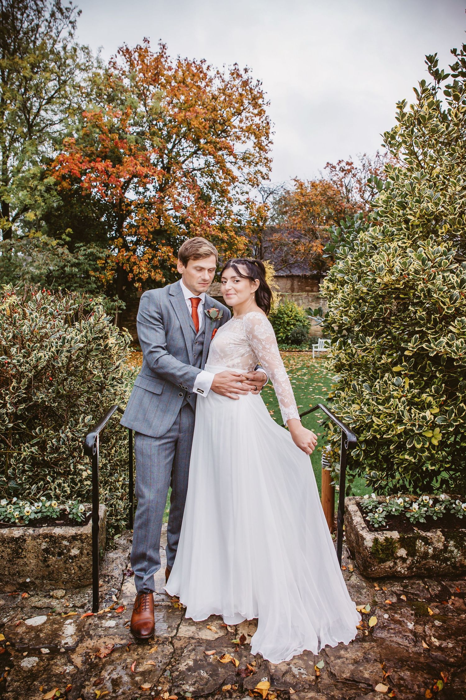 Elegant wedding portrait with couple embracing on garden steps during fall season.