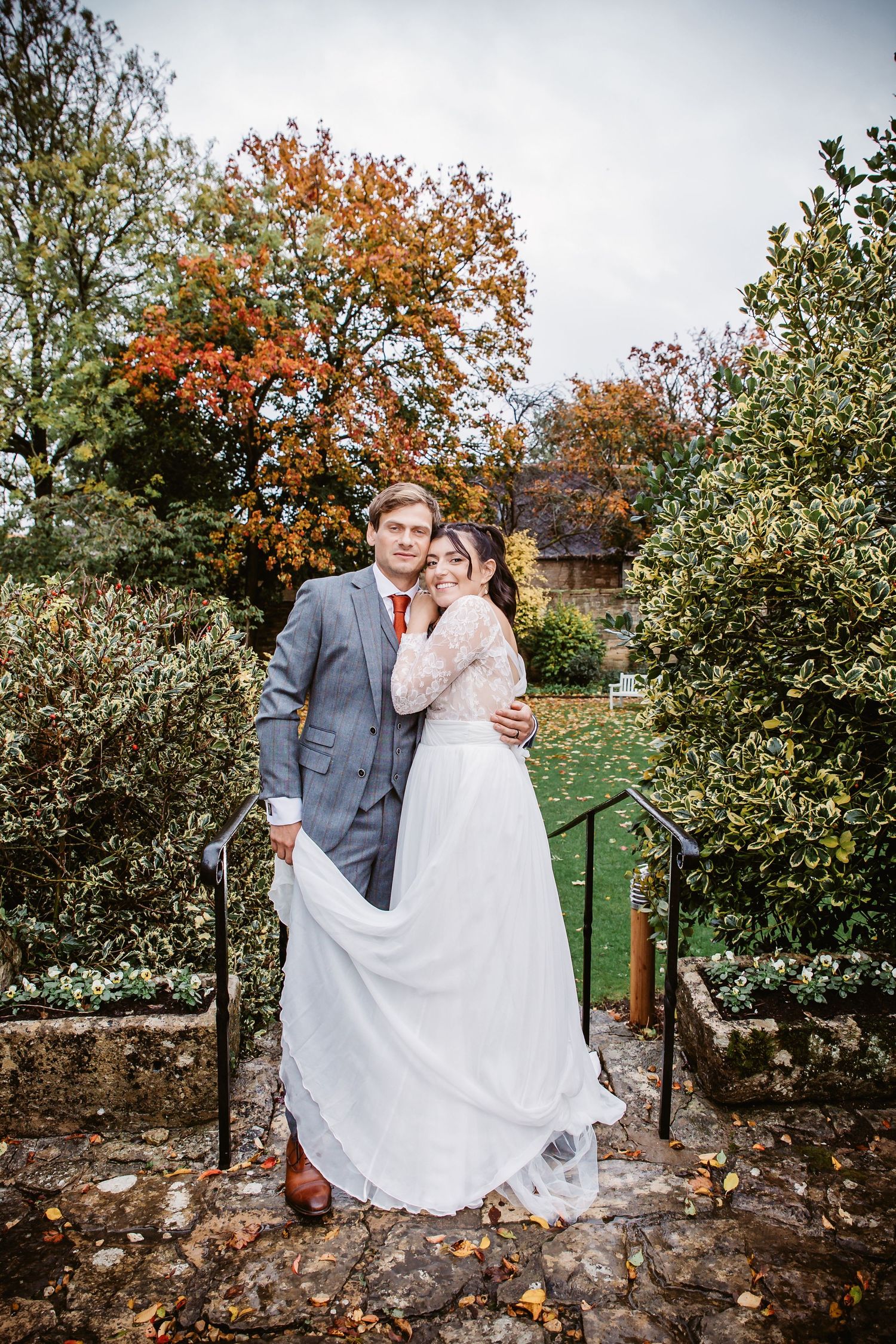 A couple poses for a romantic autumn wedding photo in front of fall foliage and stone walls.
