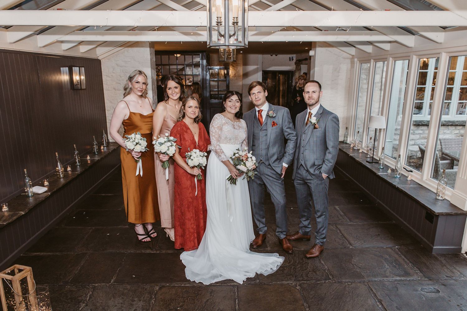 Wedding party poses together in formal attire in venue hallway with elegant lighting.
