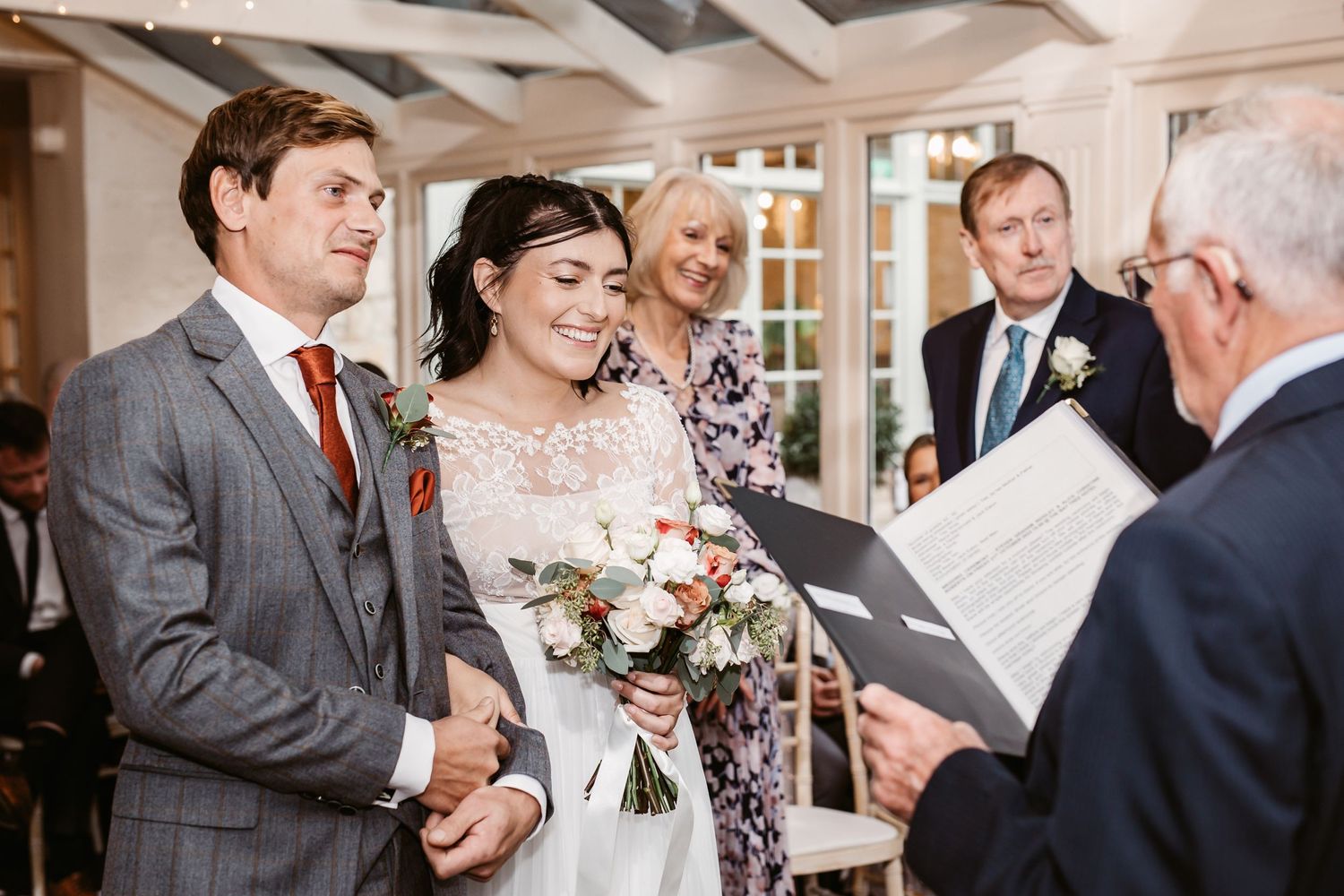 Wedding ceremony in progress with couple and officiant in bright indoor venue.