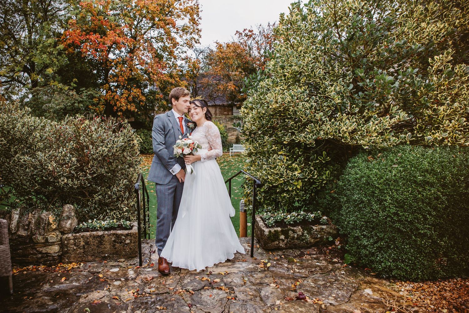 Romantic wedding portrait on garden steps with autumn colors and stone walls.