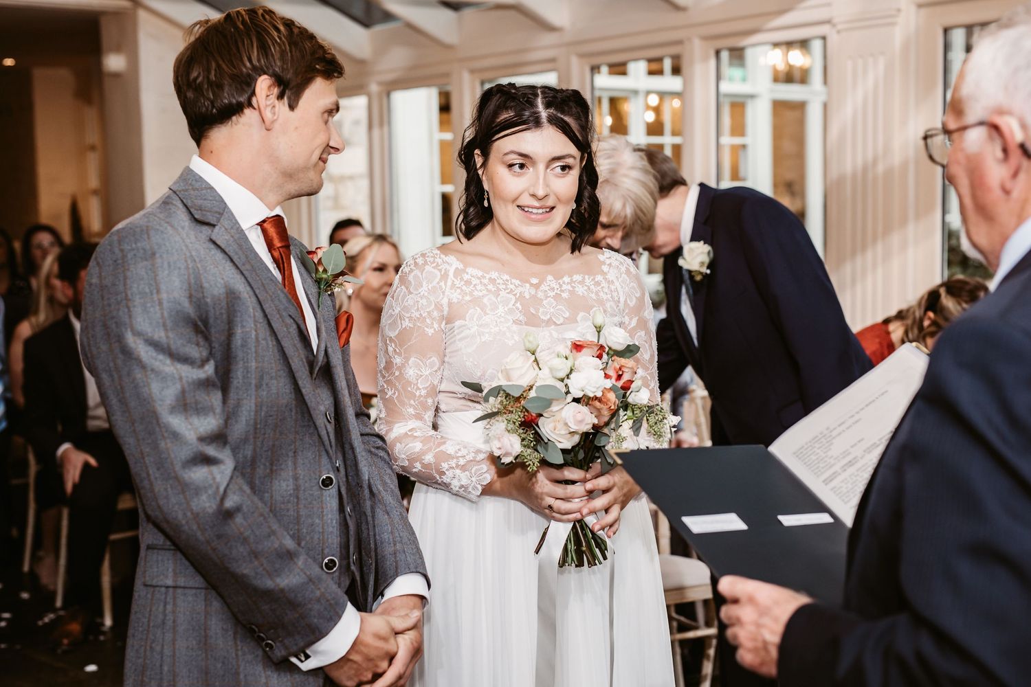 Intimate wedding ceremony moment with couple and officiant in bright indoor setting.