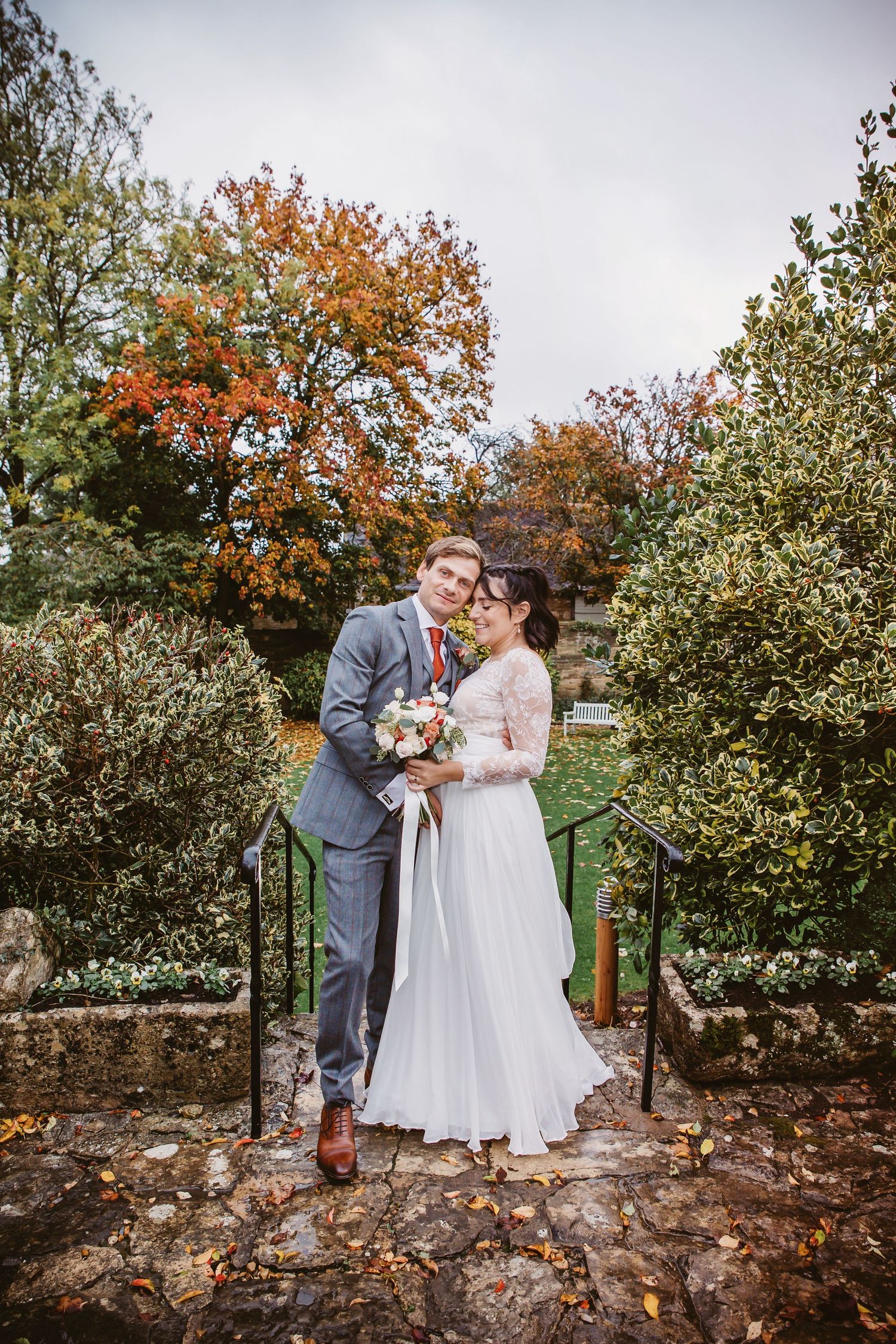 Autumn wedding portrait showing couple embracing on stone steps with vibrant fall colors.