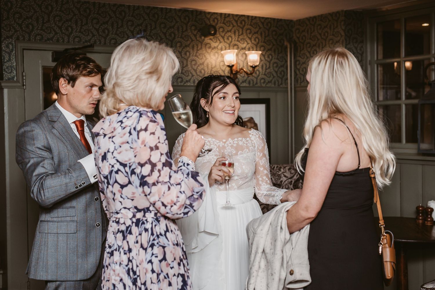 Wedding guests gathered in formal attire enjoying conversation at an indoor reception.