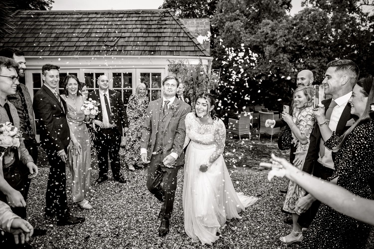 Wedding guests celebrate by throwing confetti at a garden ceremony.