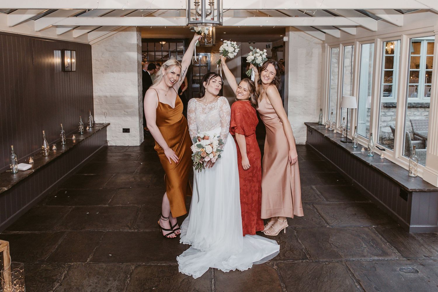 Wedding party in coordinated fall-colored dresses pose together inside luxurious venue.