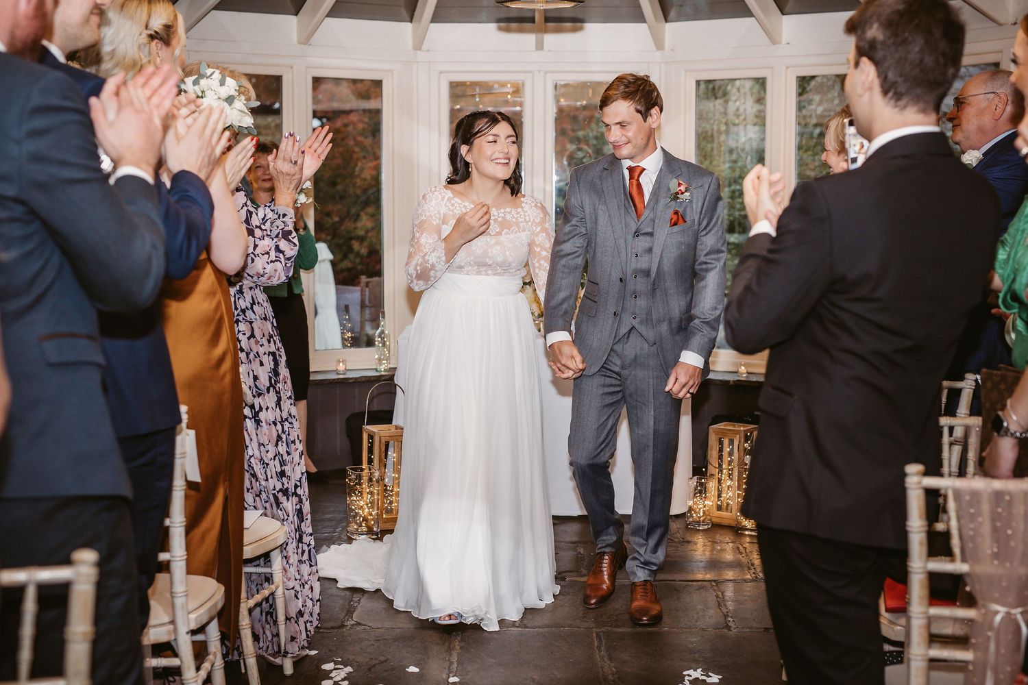 Wedding guests applaud during a celebratory moment in a light-filled venue.