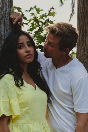Intimate portrait of a couple in white and yellow clothing among trees.