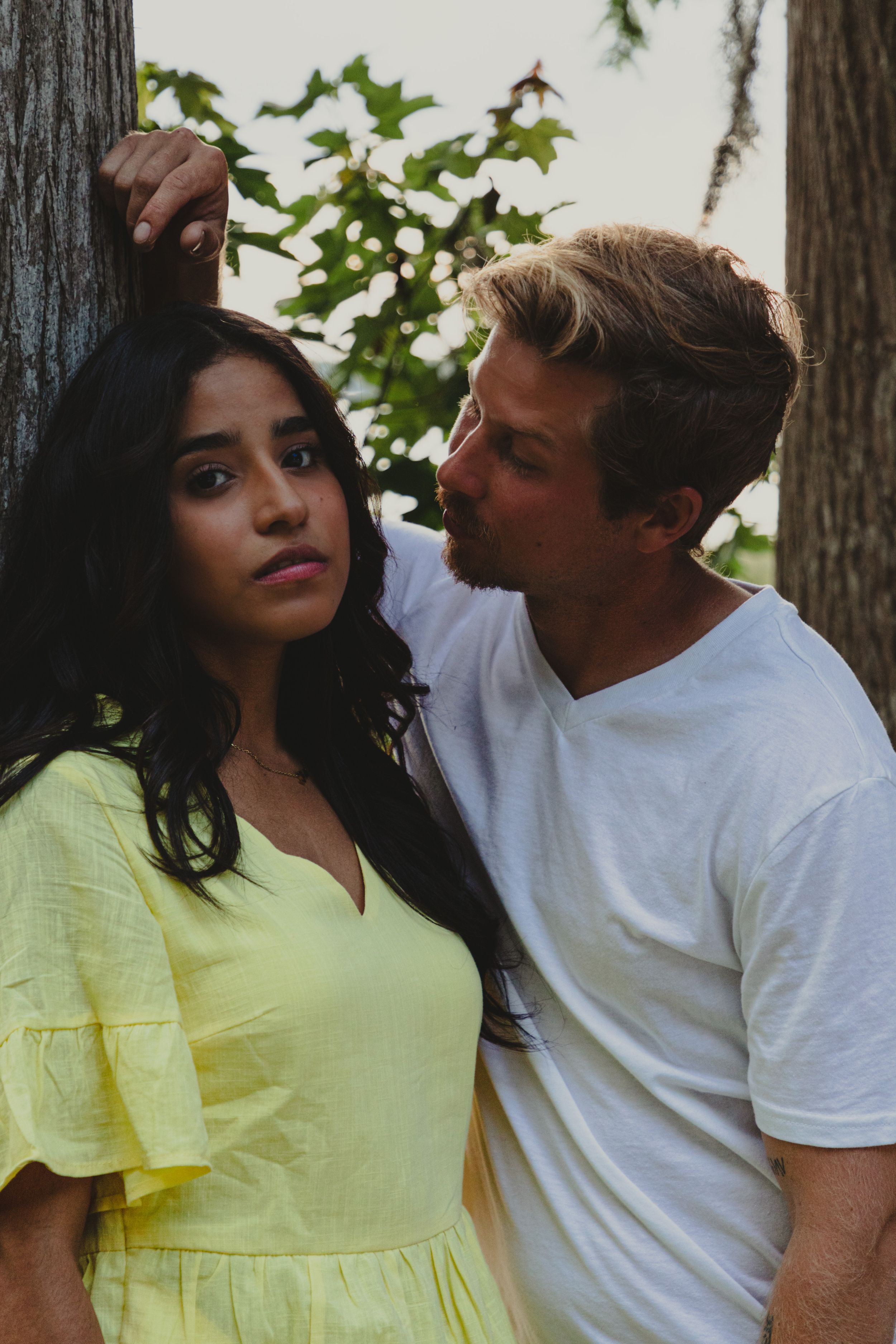 Intimate portrait of a couple in white and yellow clothing among trees.