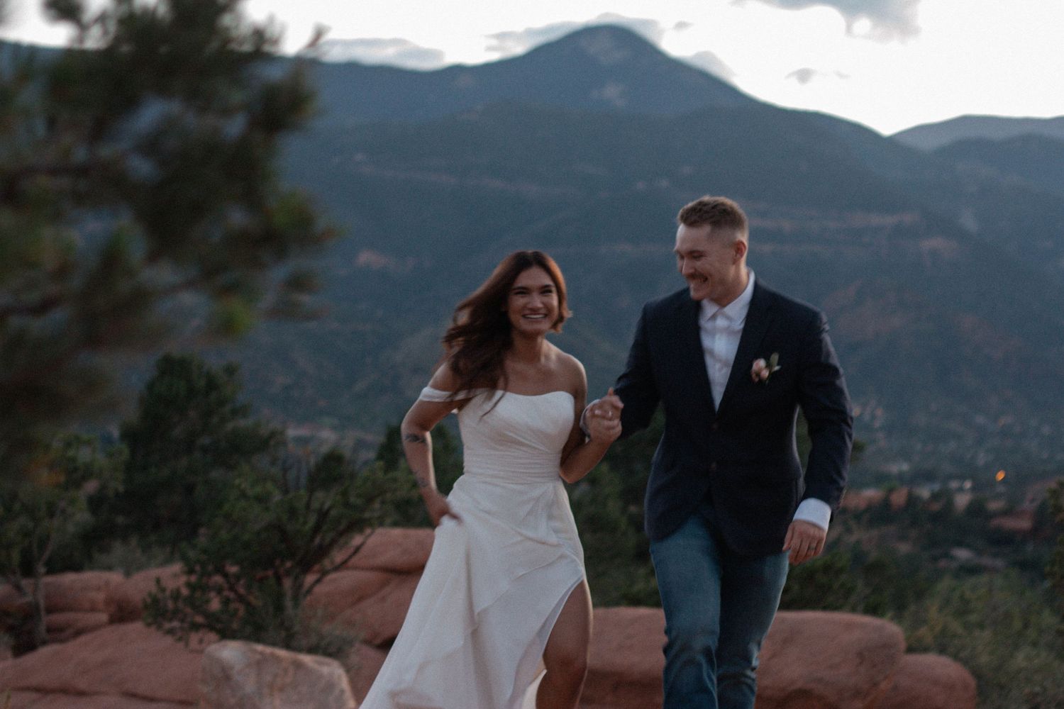 Couple in wedding attire walk together on red rocks with mountain views at Garden of the Gods in Colorado. Elopement photographer, romantic