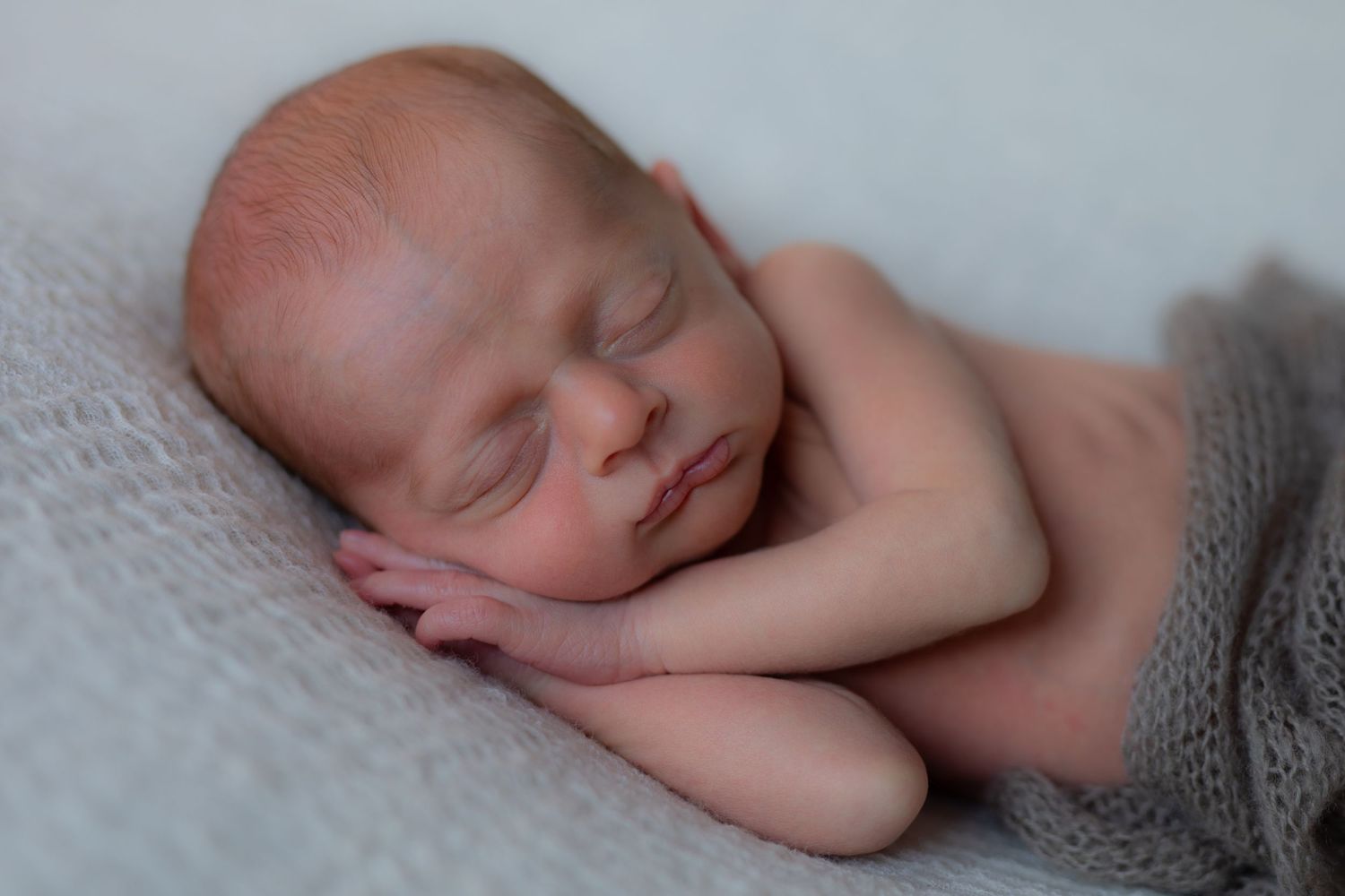 Peaceful sleeping newborn baby in soft light with gray wrap.