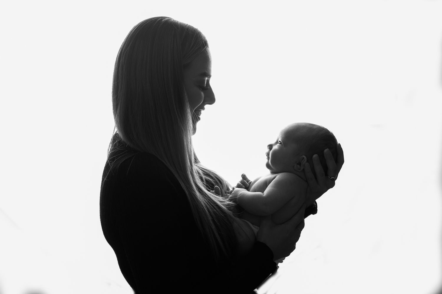 Silhouette of mother holding baby in backlit artistic portrait.
