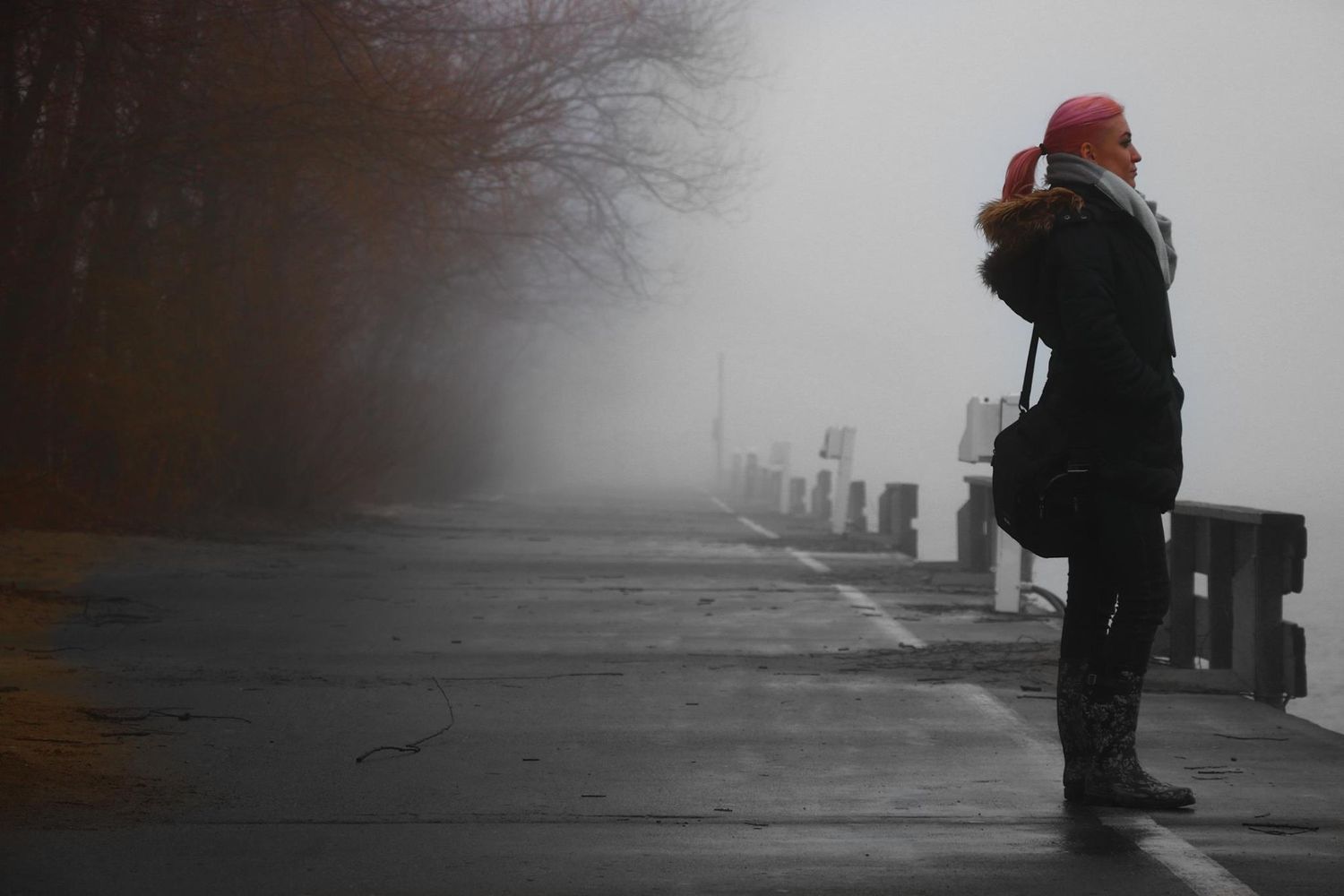 Person in red hat stands in foggy winter landscape with industrial equipment in background.