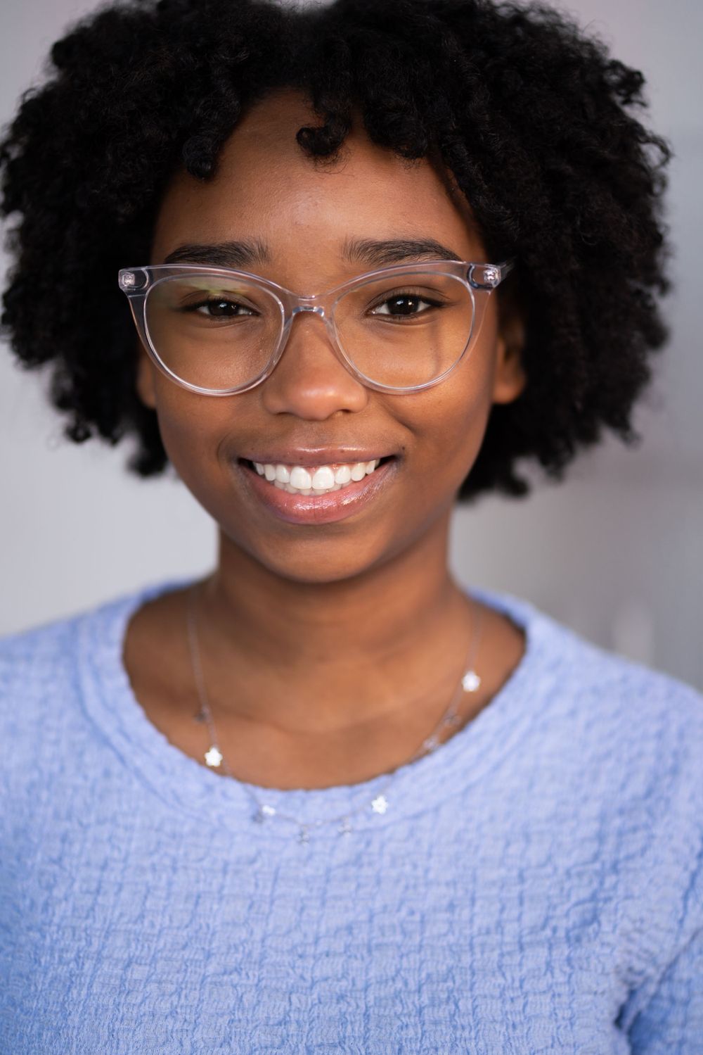 Studio portrait in soft lighting showing a light blue textured sweater and clear glasses.