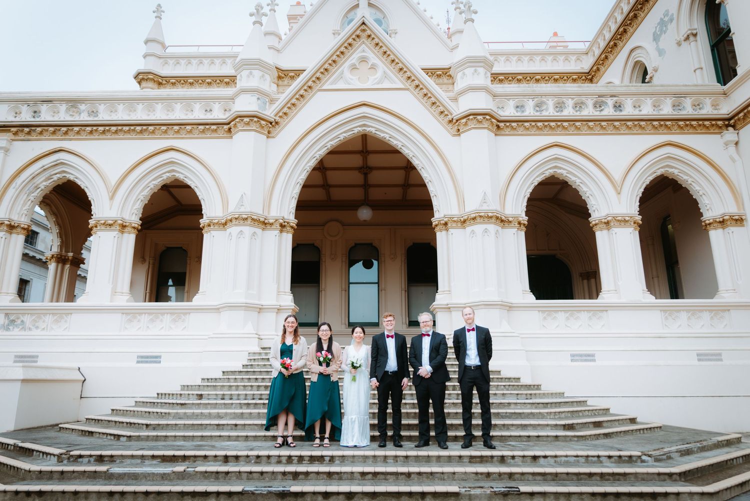 Wedding party posing on grand white steps of a historic Wellington building - elegant fine-art wedding photography.