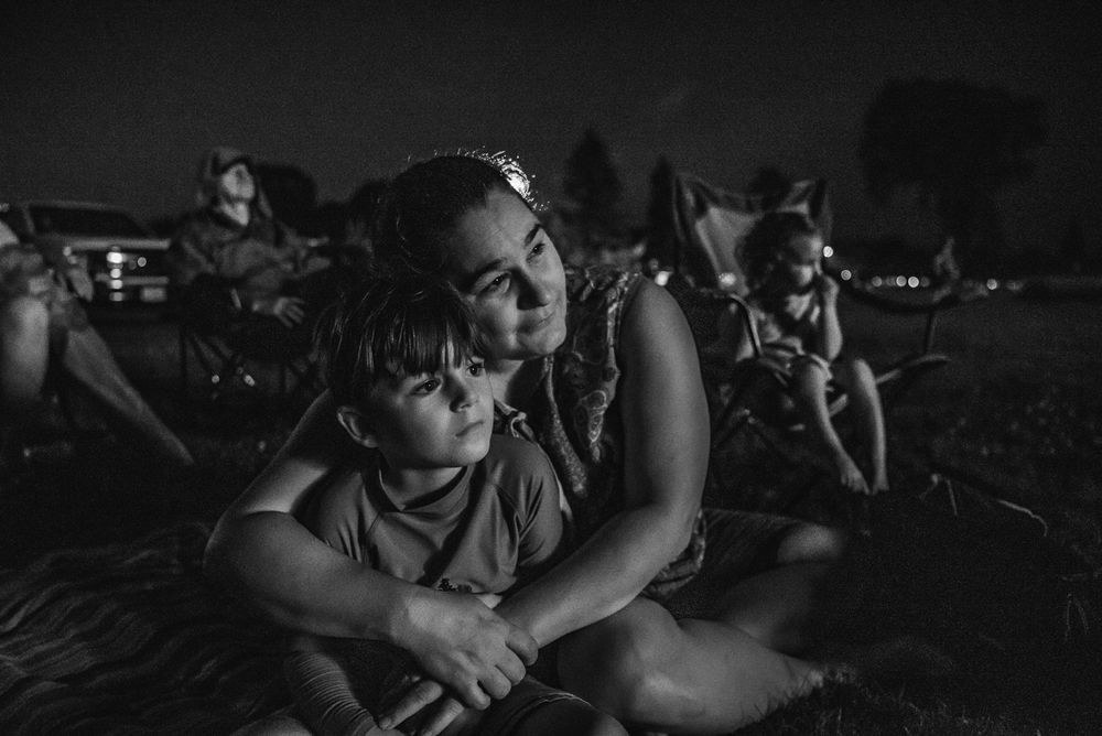 BW image of a woman with her arms around her son as they watch fireworks on Canada Day.