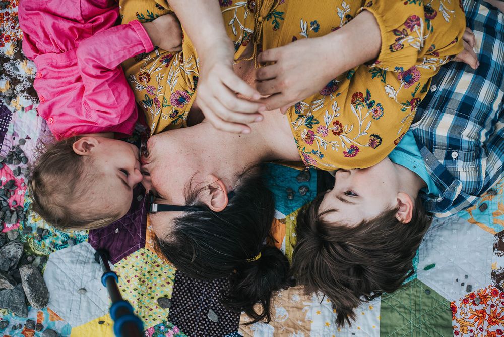 A mom lays between her young son and daughter on a patchwork quilt.