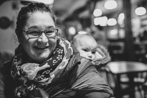 Mama baby wearing her little one on her back in a bw photo taken at a pub in Windsor ON.
