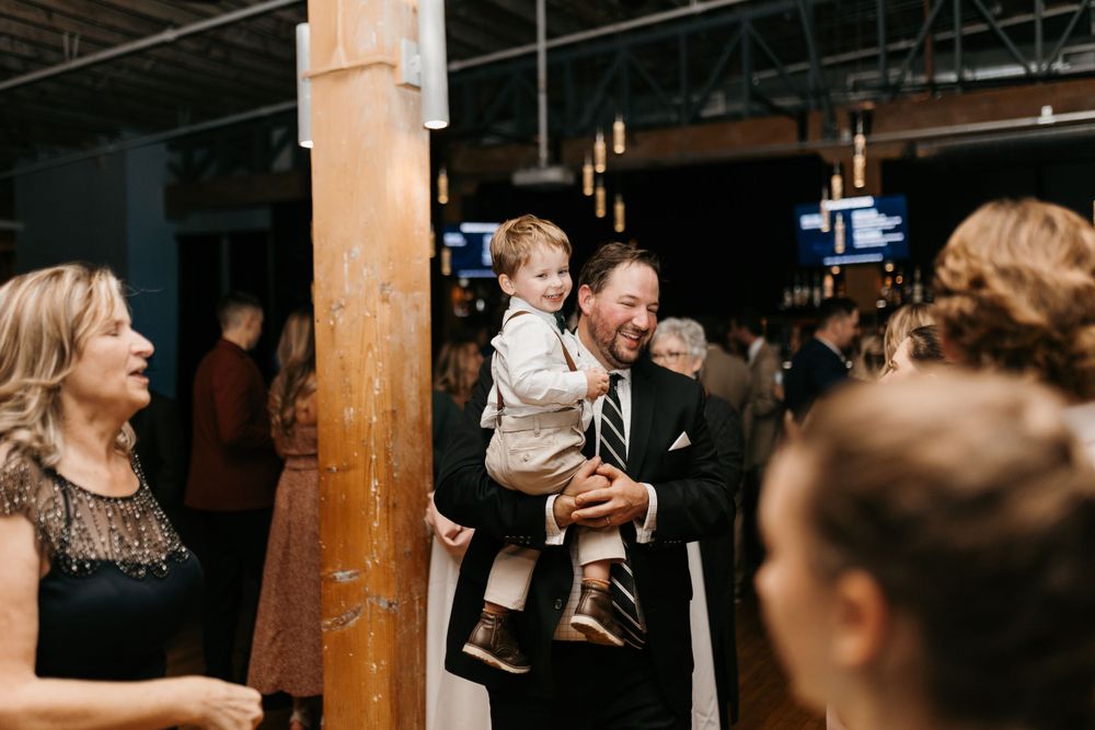Joyful man in suit holding a young child at a festive wedding reception.