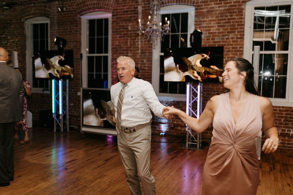 Guests dancing joyfully at a wedding reception in a rustic brick-walled venue.