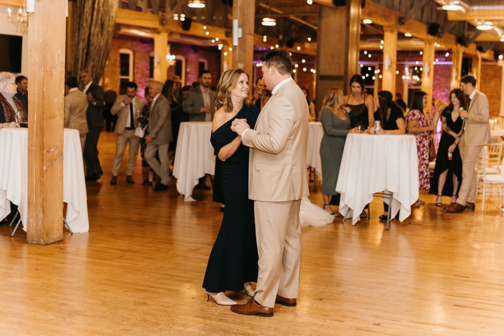 Couple sharing an elegant slow dance at a wedding reception in a rustic venue with warm lighting.