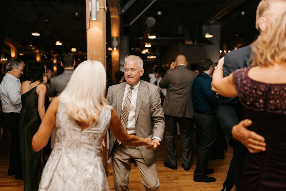 Smiling man in tan suit dancing with bride at a lively wedding reception celebration.