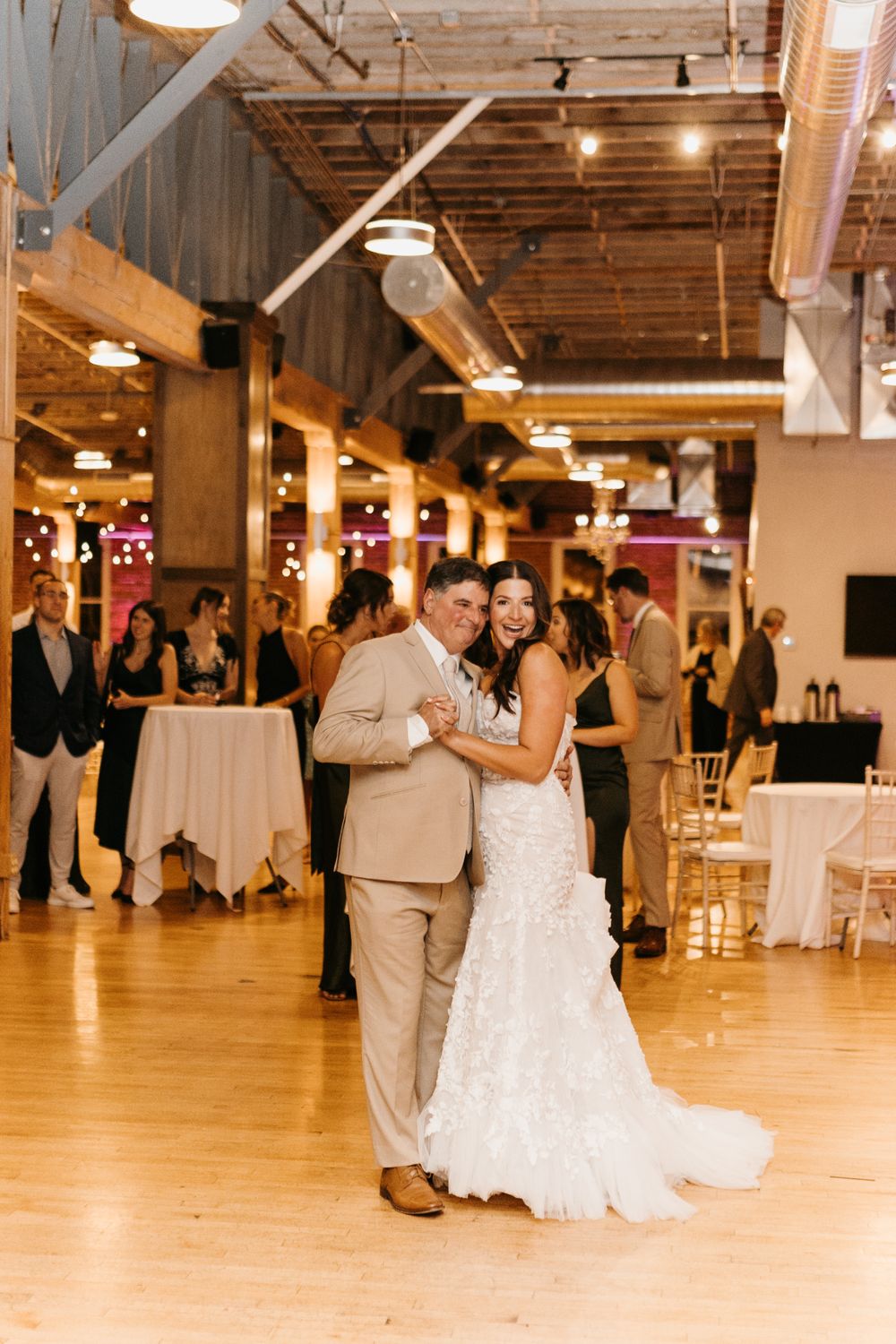 Happy bride and groom pose together on dance floor at modern industrial wedding reception venue.