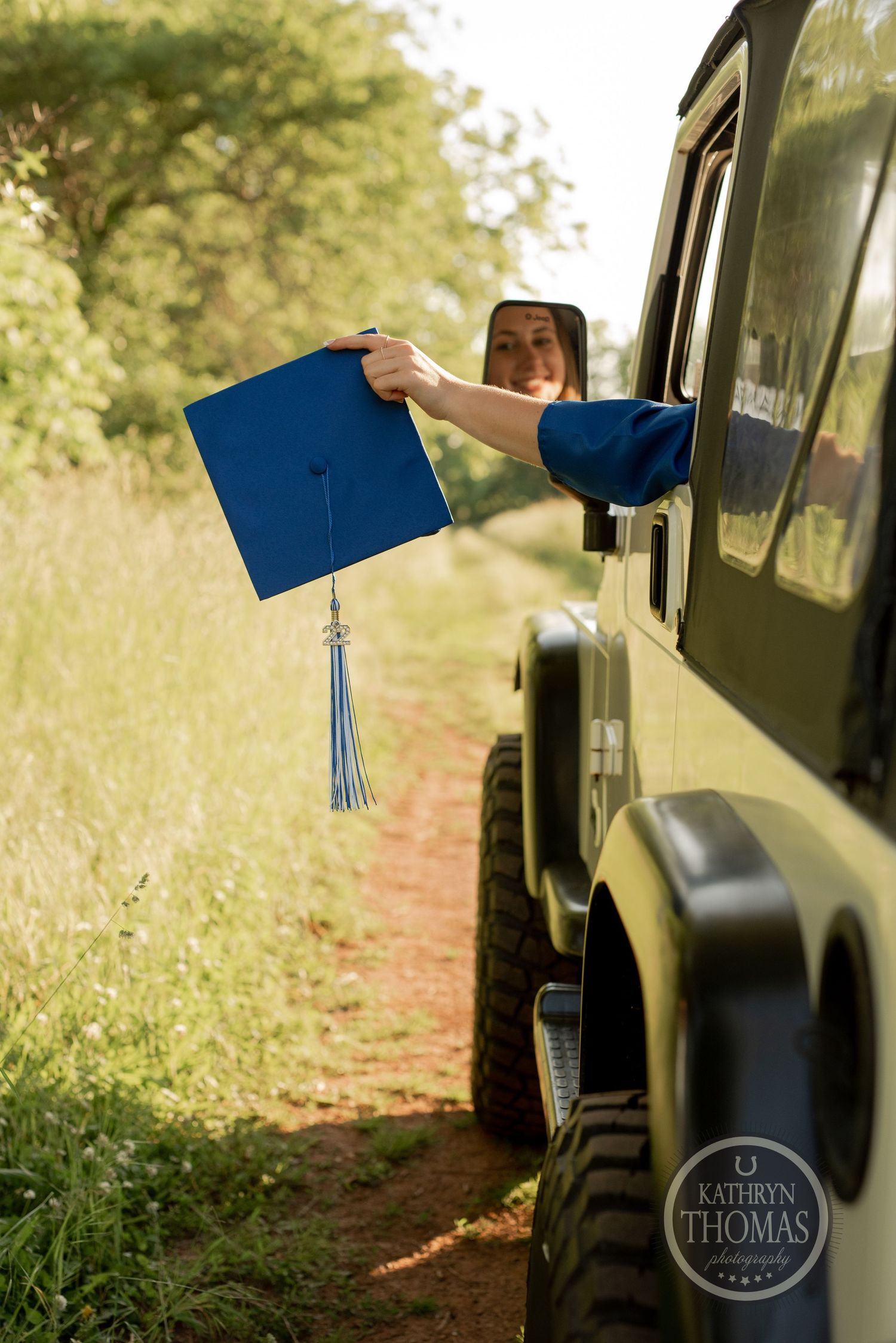Blue graduation cap with tassel held outside vintage military Jeep window.