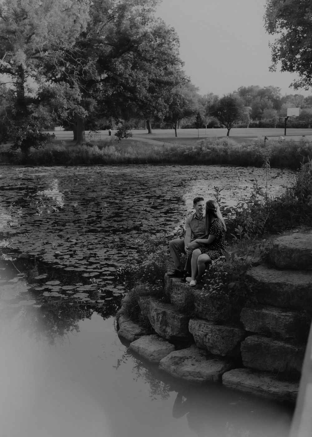 Two people sitting on stone steps by a lily pond in a park setting.