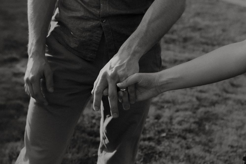 Close-up black and white shot of hands resting on legs in casual wear.