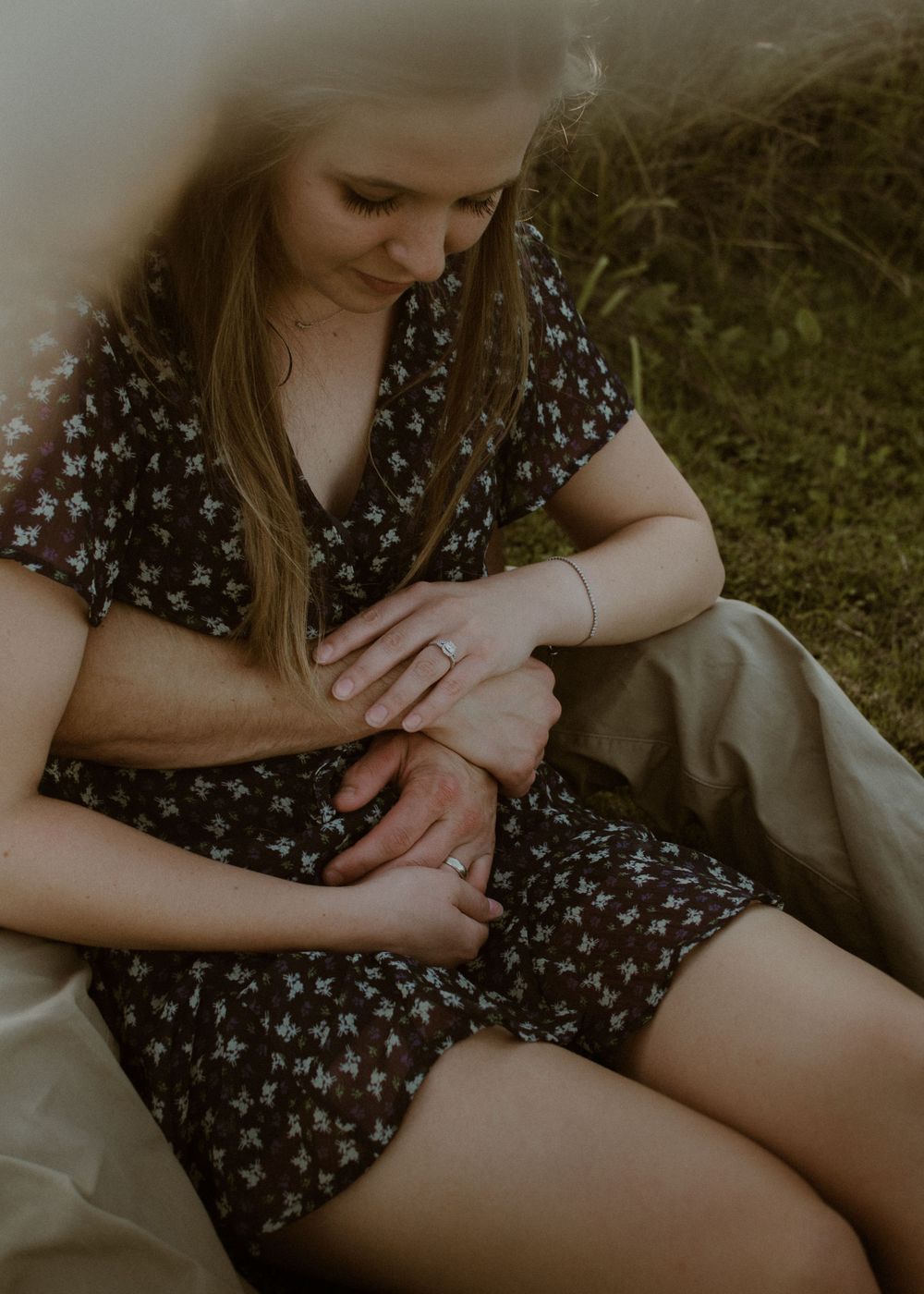 Woman in floral dress sits on blanket outdoors during golden hour.