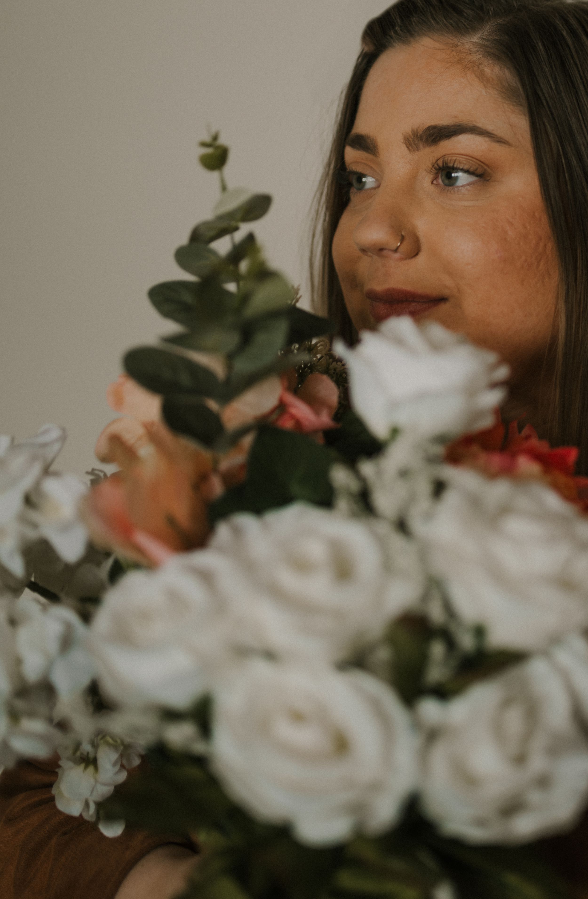 Artistic portrait with white roses and eucalyptus leaves in soft lighting.