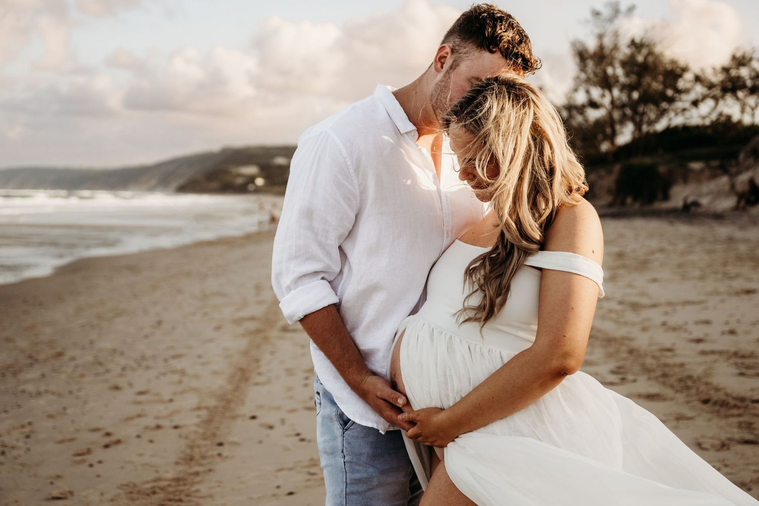 A couple embracing on a beach during golden hour with waves crashing in the background.