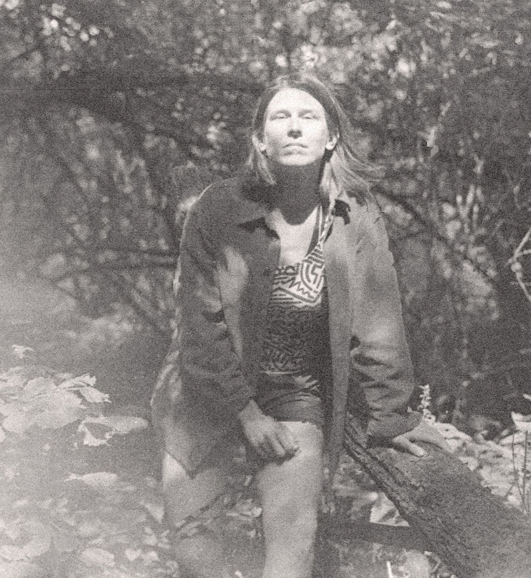 Black and white self-portrait of Anna amongst trees, a white woman in her early 40s with shoulder-length brown hair.