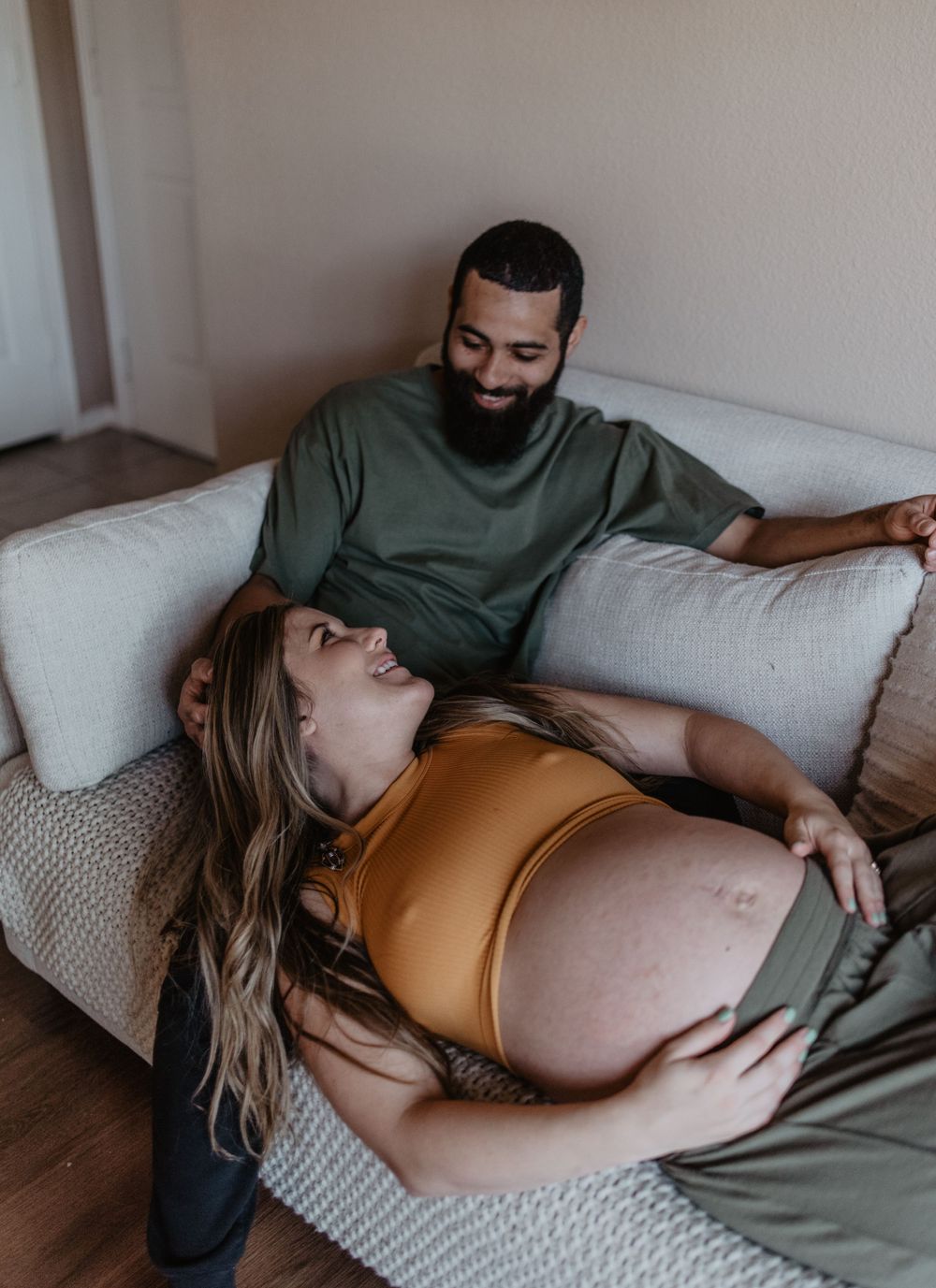An intimate maternity portrait showing a couple sharing a moment on their white couch.