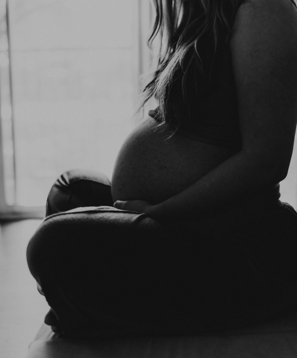 Silhouette of pregnant belly against window light in black and white photography.