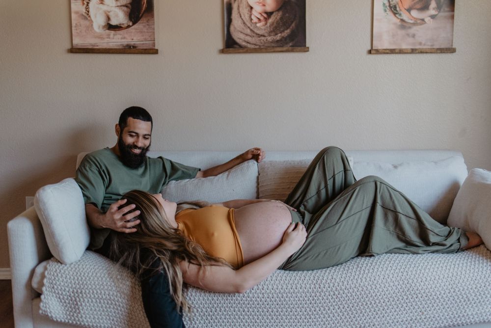 A relaxed maternity moment captured on a white couch in a living room setting.