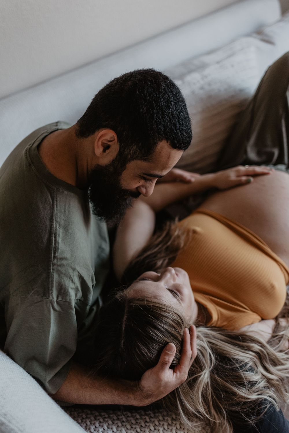 Intimate moment captured between couple during pregnancy photoshoot on white bedding.