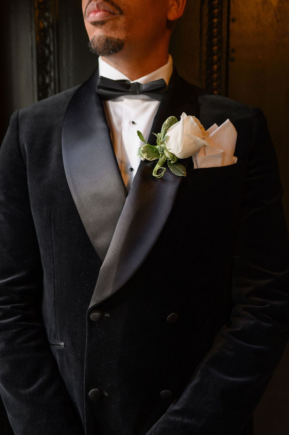 Close-up of a black velvet tuxedo with white rose boutonniere and bowtie.