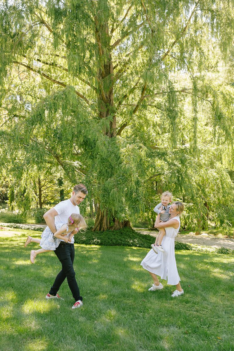 a couple plays with their two young kids in their Greenwich, CT backyard against a willow tree, photo by Paula Ortiz NYC