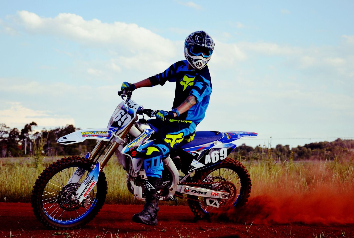 Dirt bike rider in blue gear performing a jump on a dusty track.