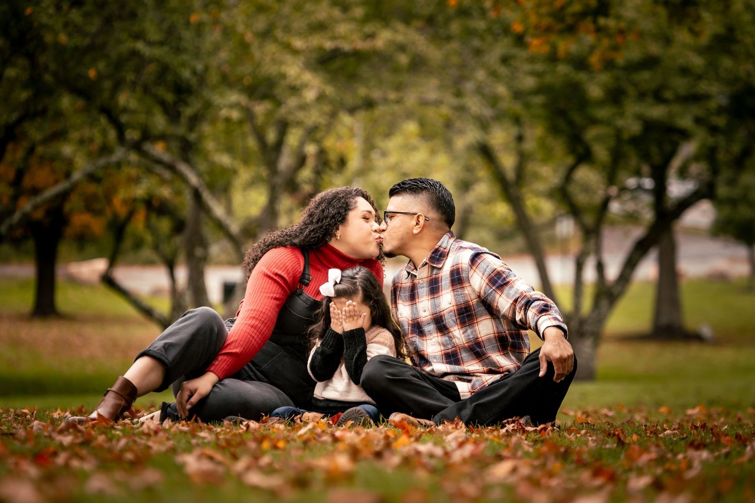 Couple sitting on autumn leaves in park during romantic photoshoot.