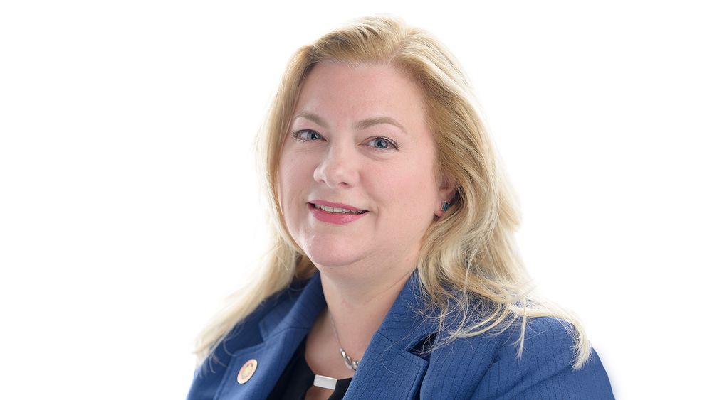 Professional headshot of a person in a blue blazer against a light background.