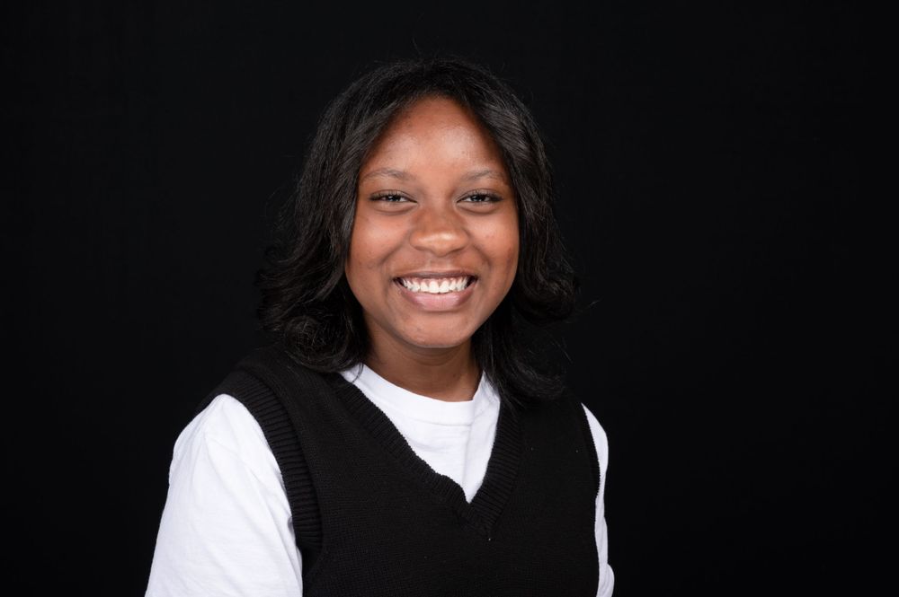 Professional portrait of person in black vest and white shirt smiling warmly.