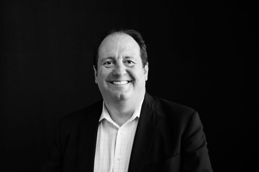 Professional headshot of person in business attire smiling against black background.