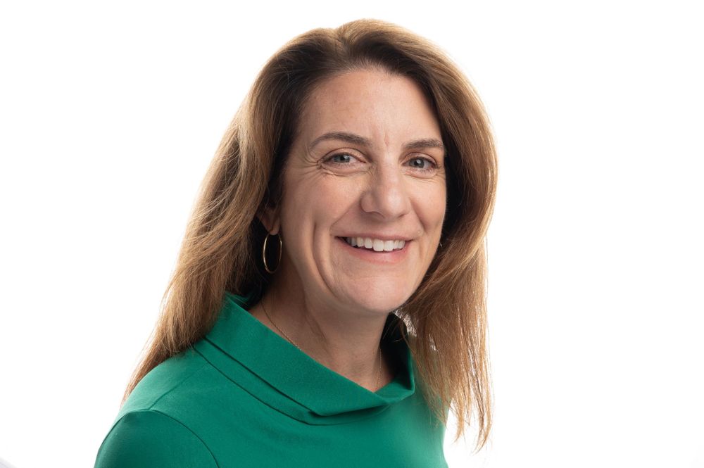 Professional headshot in green turtleneck against light background.